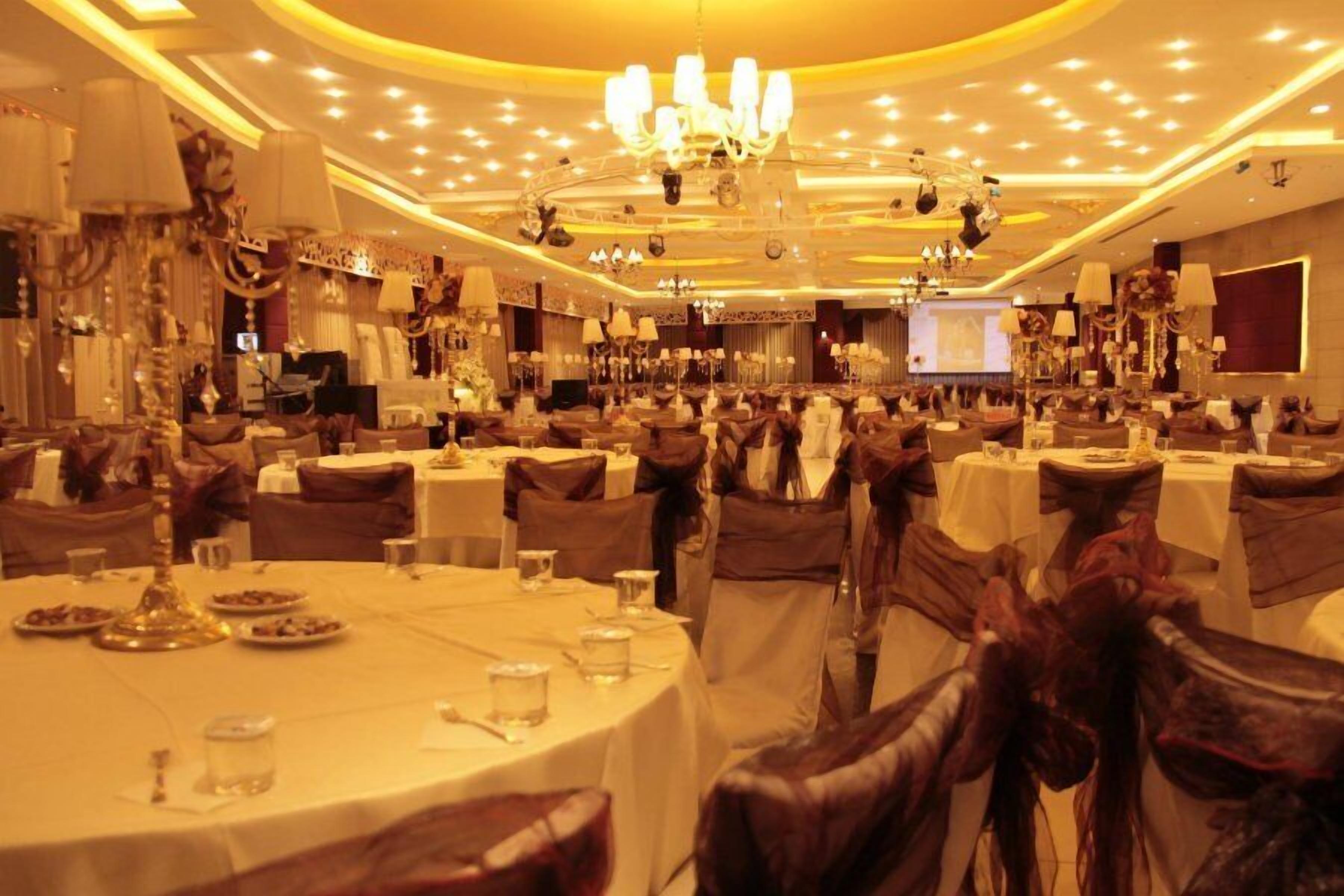 Uma sala de banquetes com mesas redondas, cadeiras e lustres.