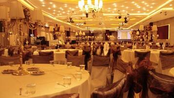 Uma sala de banquetes com mesas redondas, cadeiras e lustres.