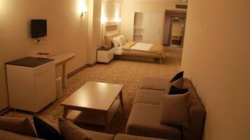 Et lille hotelværelse med seng, sofa, lille bord, skrivebord og fjernsyn.