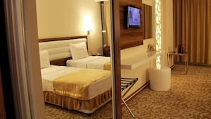 A hotel room with two beds, a TV mounted on the wall, a small table, and a decorative wall panel. - Ozpark Hotel (Aksehir)