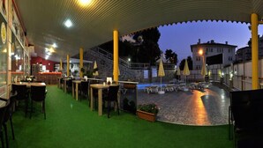An outdoor dining area with tables and chairs, a covered seating area, and a view of the cityscape in the background. - Ali Unal Apart Otel (Alanya)