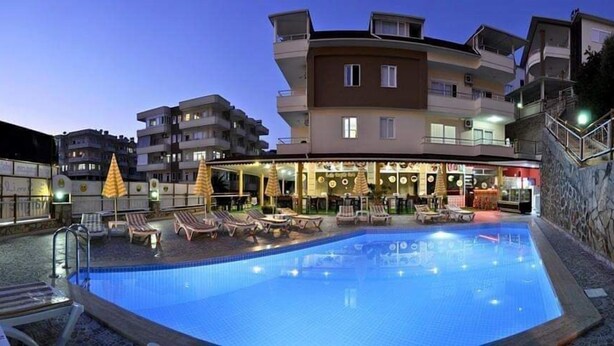 A swimming pool with lounge chairs and umbrellas, surrounded by multi-story buildings. - Ali Unal Apart Otel (Alanya)