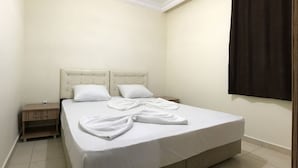 A neatly made bed with white linens and two pillows, a wooden nightstand with a lamp, and a dark curtain on the window. - Ali Unal Apart Otel (Alanya)