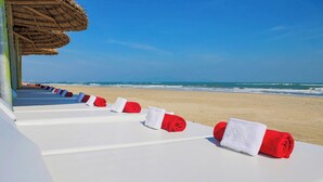 A beachside hotel with white lounge chairs and red towels, a thatched roof structure, and a view of the ocean. - Lantana Riverside Hoi An Hotel (Da Nang)