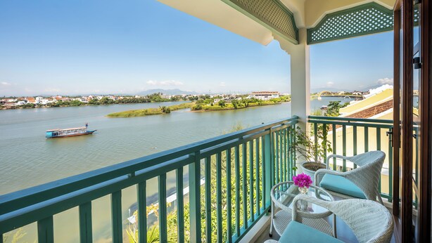 A balcony with wicker furniture, a view of a river, and a distant boat. - Lantana Riverside Hoi An Hotel (Da Nang)