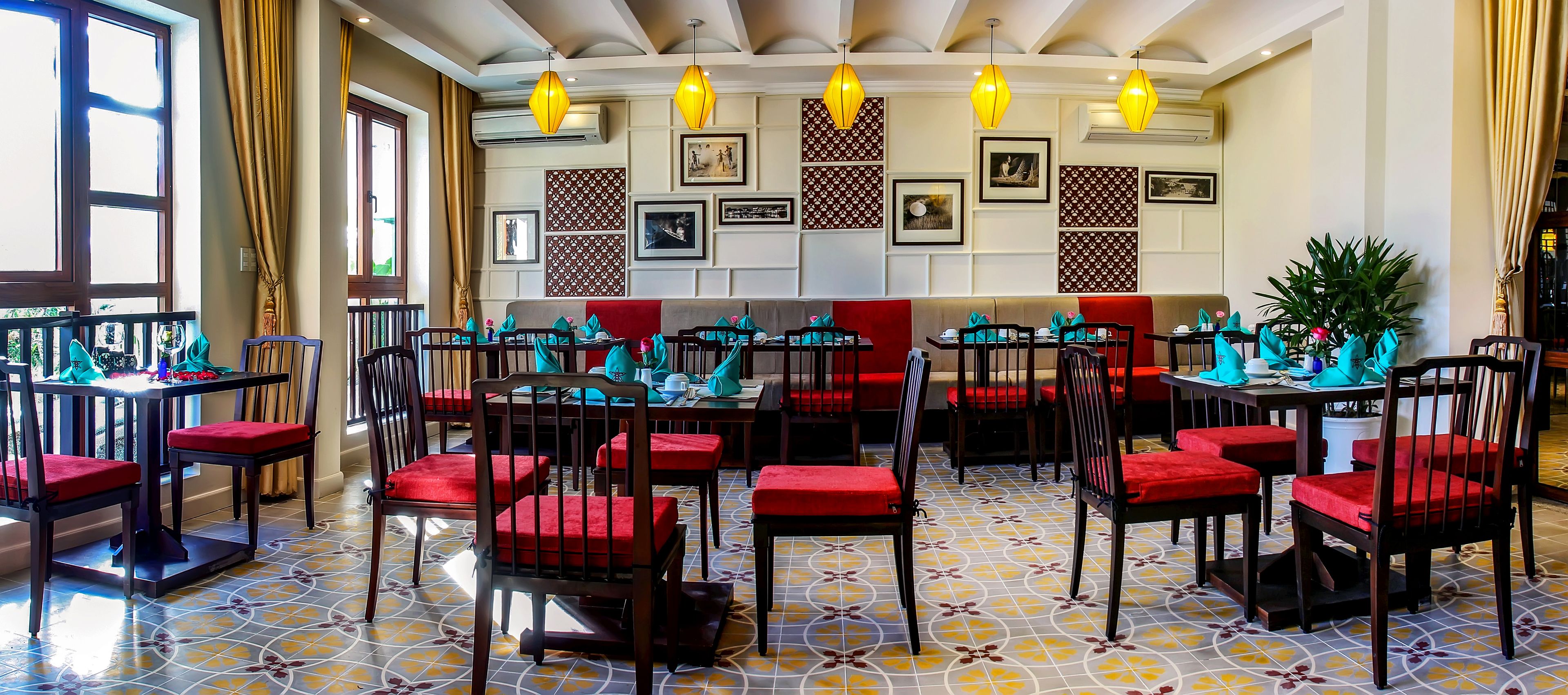 A restaurant with red cushioned chairs and tables, yellow pendant lights, and patterned wall decorations.