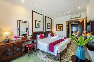 Habitación de hotel con dos camas, un escritorio, una silla, tocador con espejo y un florero con flores.
