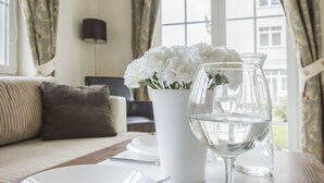 Una habitación con un sofá blanco, un florero con flores blancas y un vaso de agua sobre una mesa.