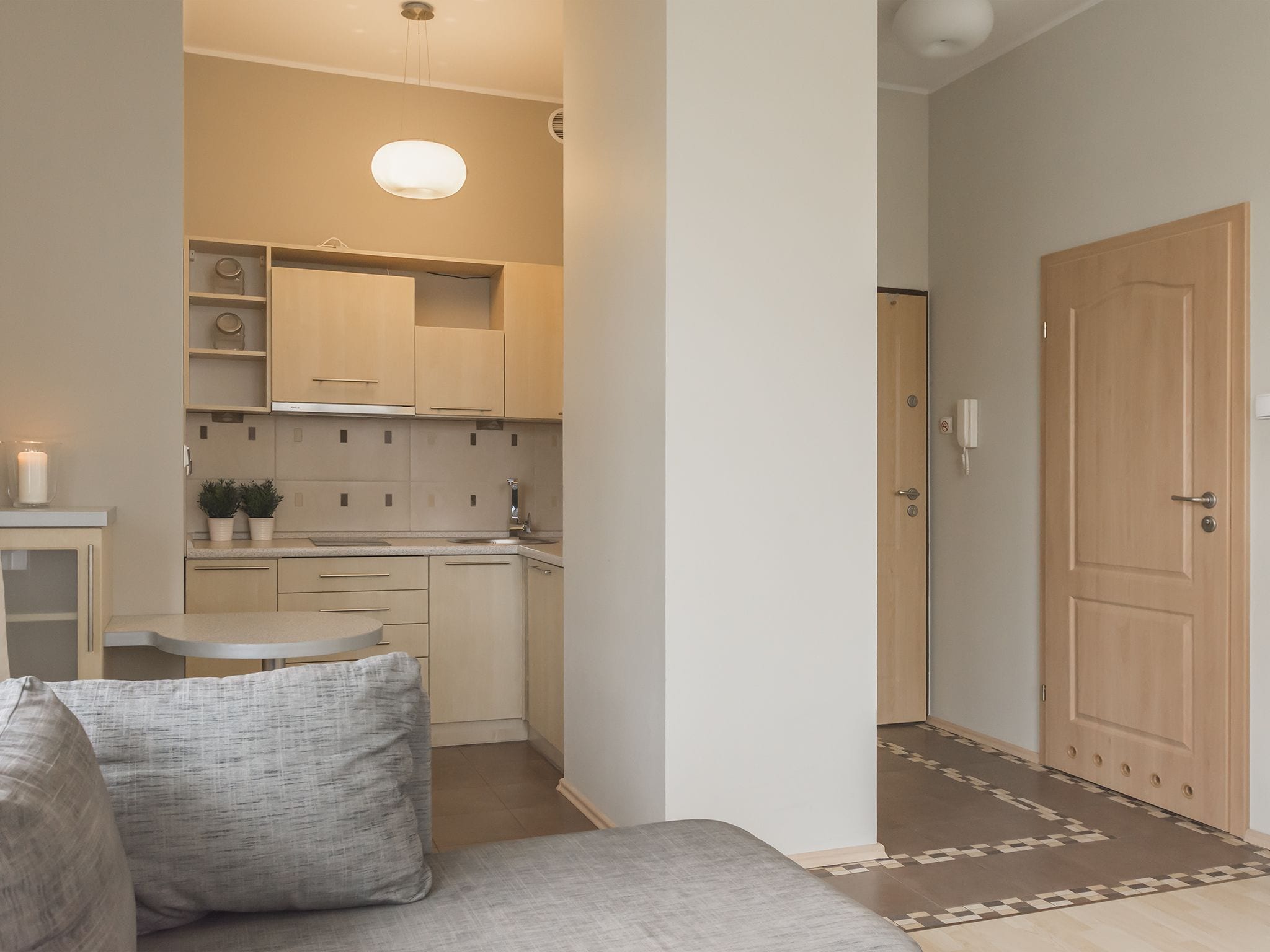 Ett kompakt bostadsutrymme med ett litet kök, en soffa med kuddar och en mönstrad matta.