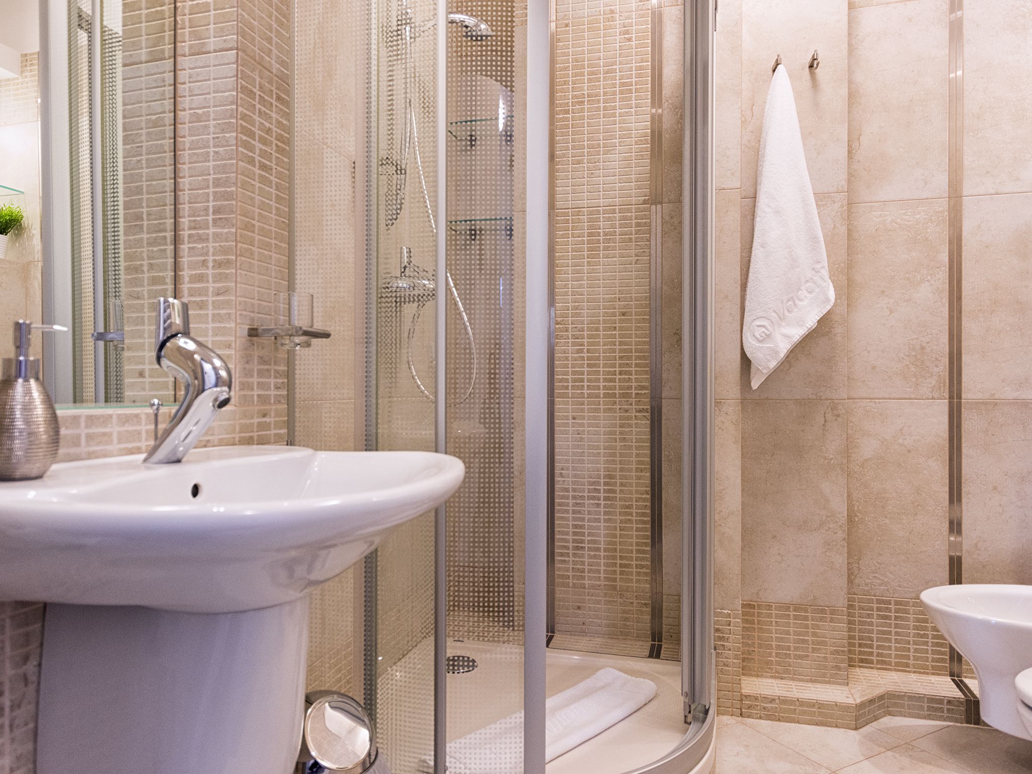 Een moderne badkamer met een douche met glazen wand, een wit wastafelmeubel en een handdoek aan de muur.