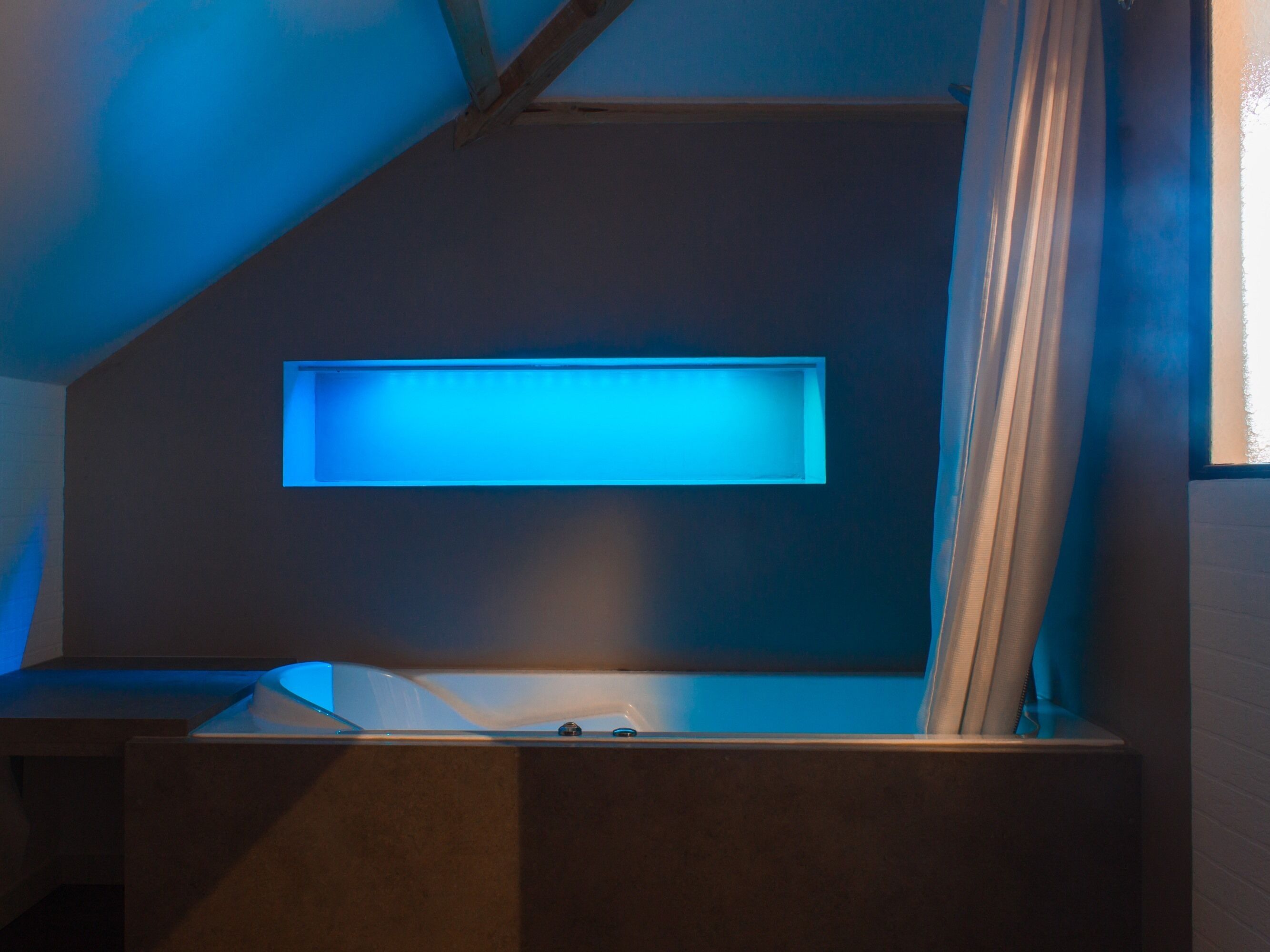 Una habitación moderna con techo inclinado, estante empotrado y ventana con cortinas.