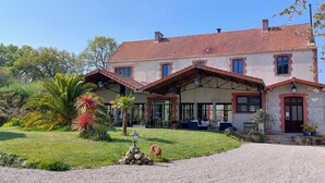 Een herenhuis met een rood pannendak, grote ramen en een verzorgde tuin met diverse planten en een kleine fontein.