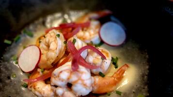 Un plat composé de crevettes, de fines tranches de radis et d’oignons verts, servi dans une assiette foncée.