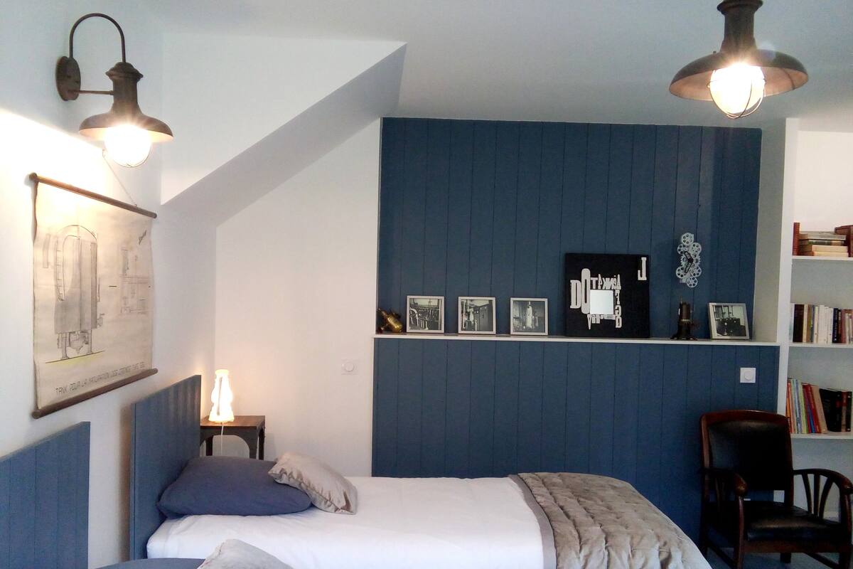 Une chambre à coucher comprenant un lit, une chaise, une étagère avec des photos et un luminaire fixé au mur.