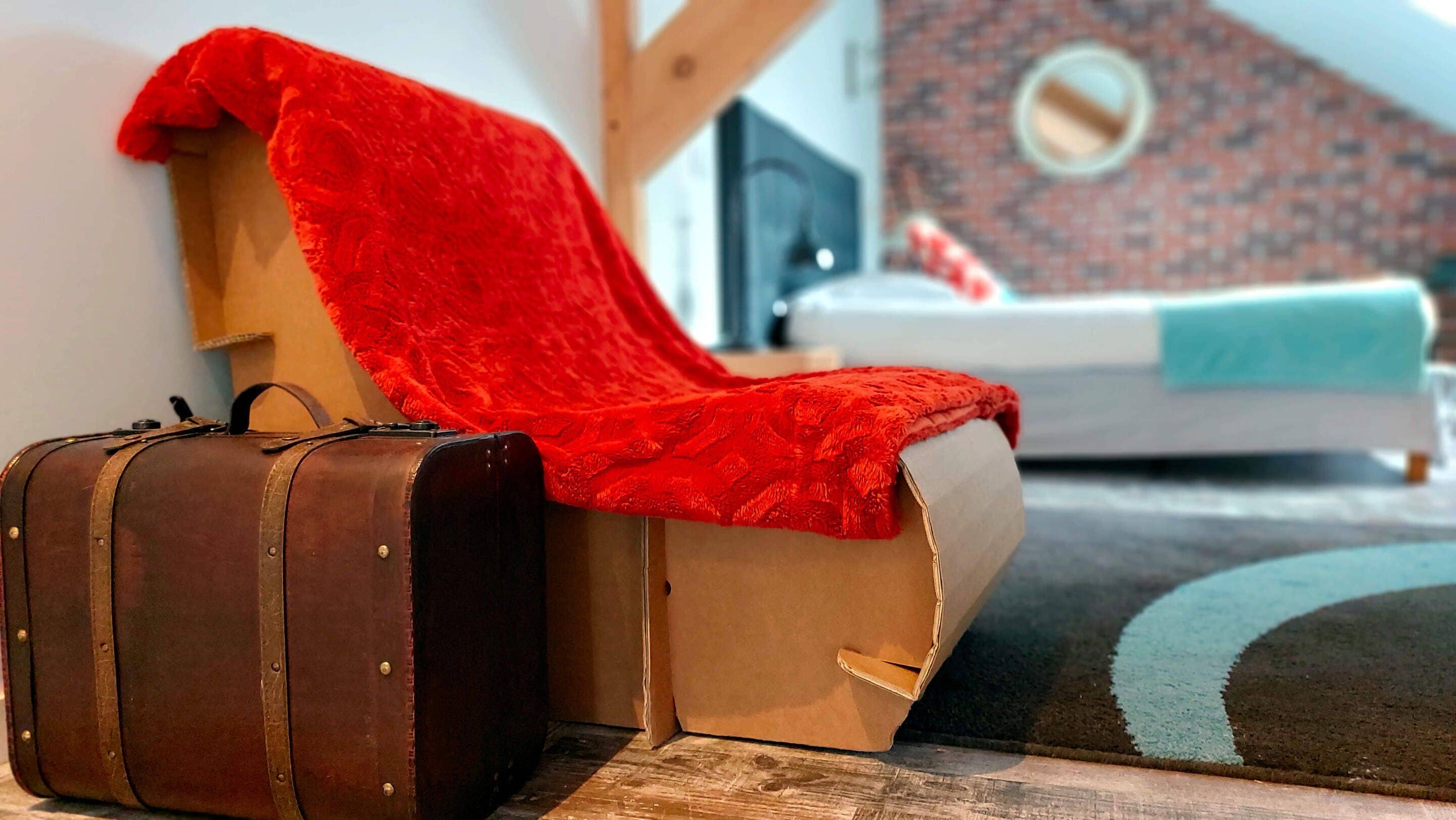 A room with a bed, a red blanket on a chair, and a suitcase on the floor.