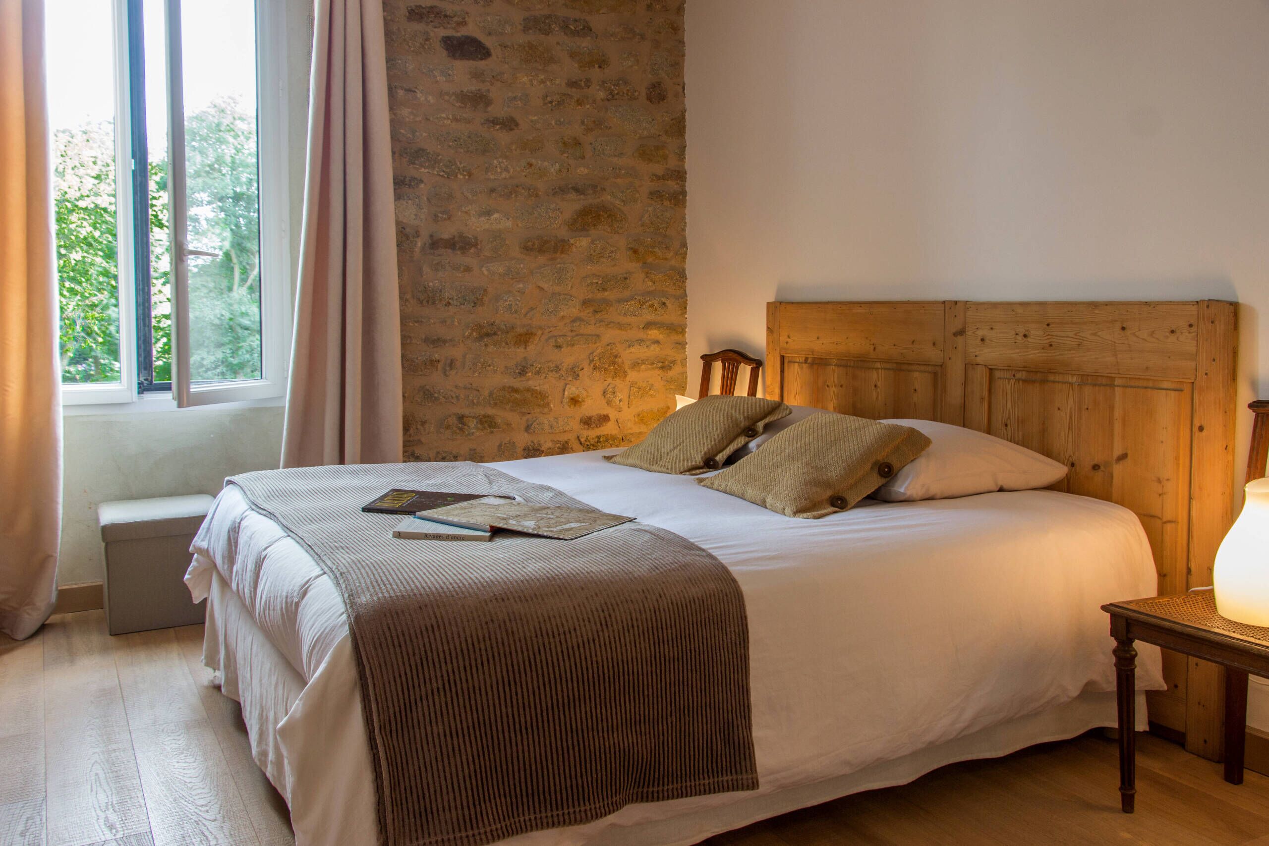 Una cama con cabecera de madera, una mesita de noche con lámpara y una ventana con cortinas.