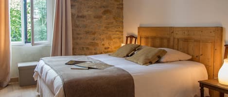 Una cama con cabecera de madera, una mesita de noche con lámpara y una ventana con cortinas.