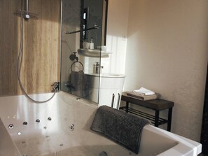 Une salle de bain moderne avec une douche à parois de verre, une baignoire blanche et une petite table avec des serviettes.