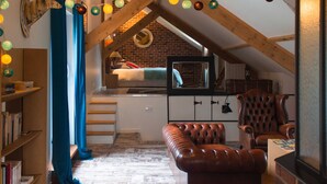 Een knus slaapkamer onder het dak met een hoogslaper, een televisie, een leren fauteuil en een boekenplank.
