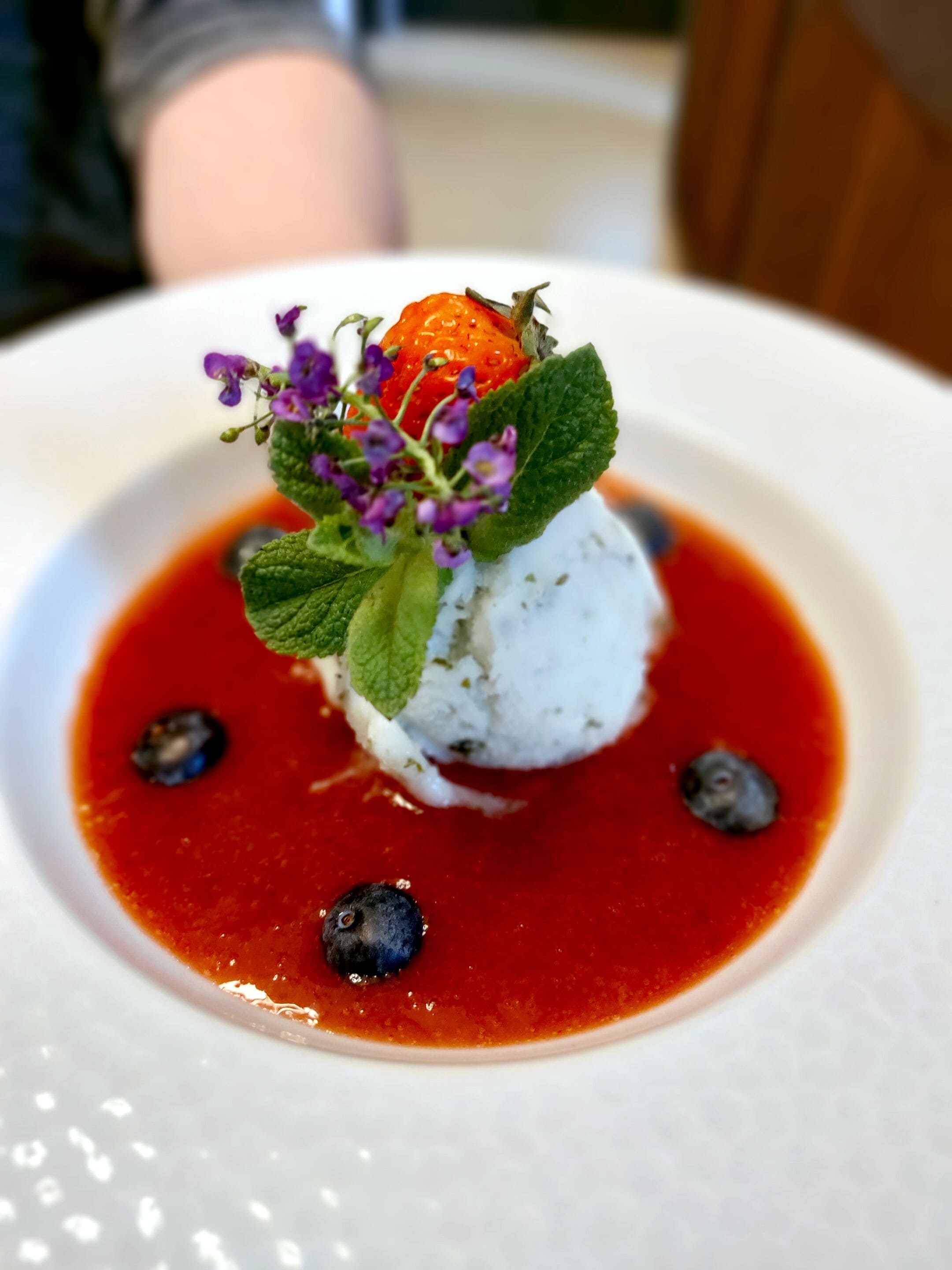 Un postre con una baya encima, rodeado de salsa roja y arándanos.