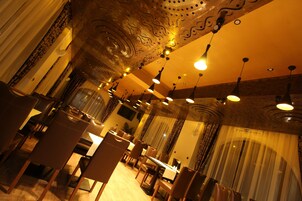 Uma sala de jantar com várias mesas e cadeiras, design de teto ornamentado e luminárias pendentes.