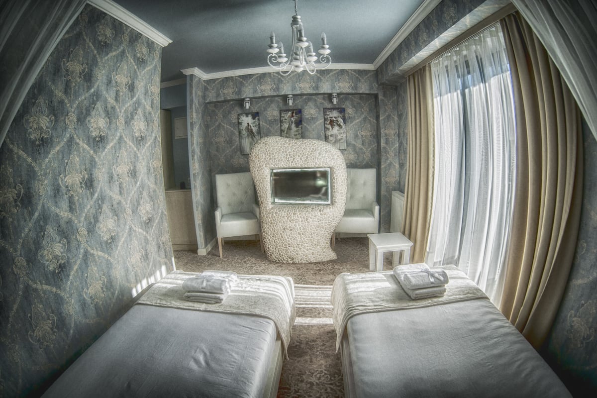 A room with two beds, a large mirror, and a seating area with a chaise lounge and armchairs.