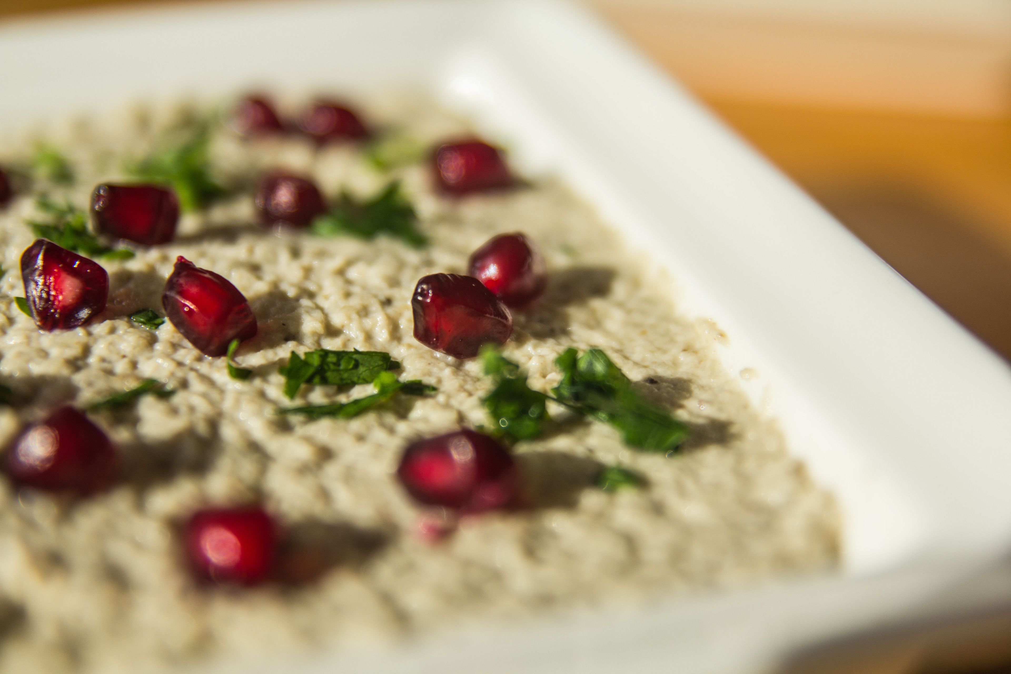A close-up of a dish with a creamy texture, garnished with red pomegranate seeds and green herbs.