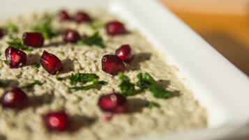 A close-up of a dish with a creamy texture, garnished with red pomegranate seeds and green herbs.