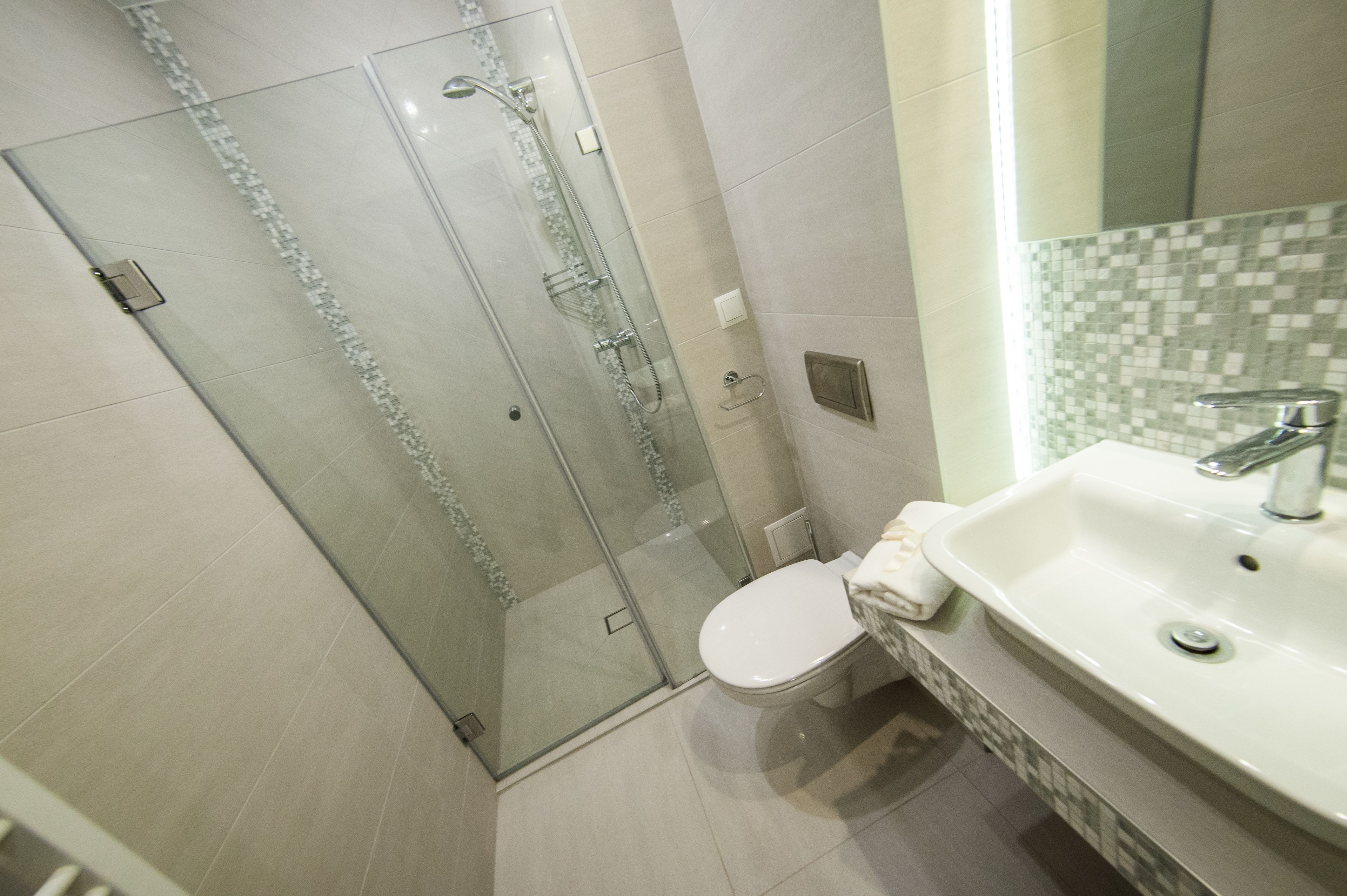 A modern bathroom with a glass-enclosed shower, a white toilet, and a sink with a tiled backsplash.