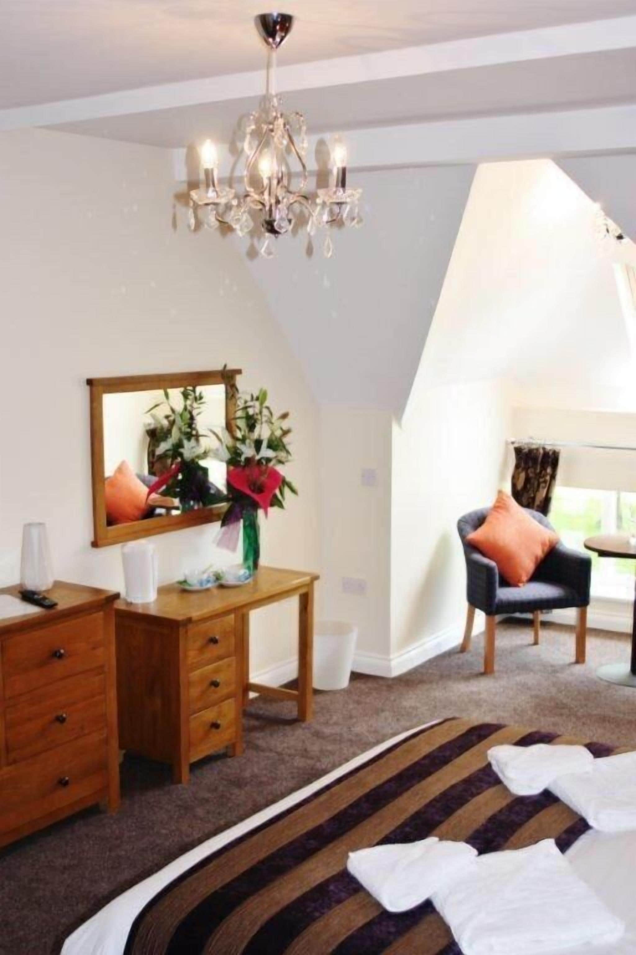 A bedroom with a wooden dresser, a mirror, a chandelier, a chair, and a striped rug.