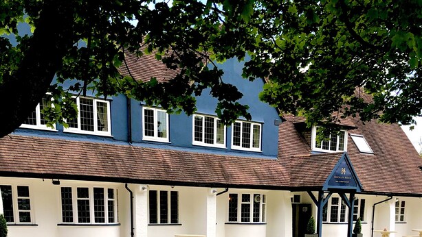 A building with a blue exterior, multiple windows, and a covered outdoor seating area with chairs and tables. - Hockley House (Solihull)