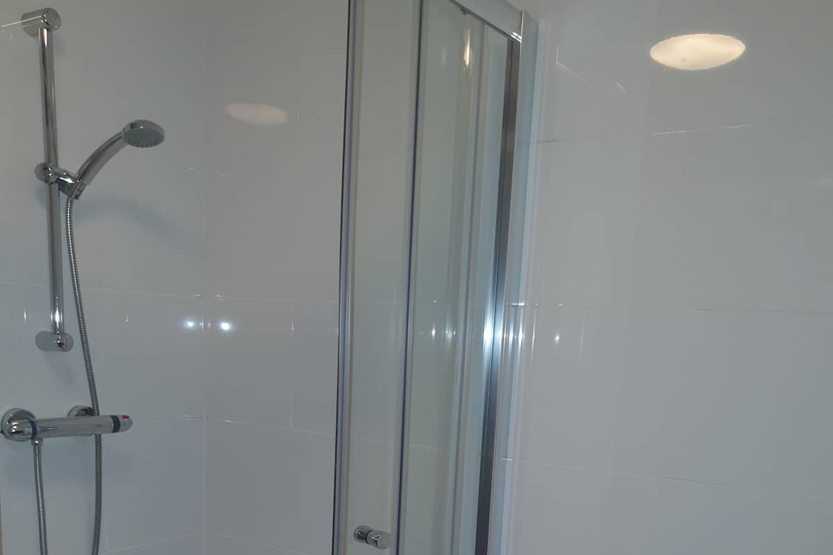 A bathroom with a glass-enclosed shower, a toilet, and tiled walls.