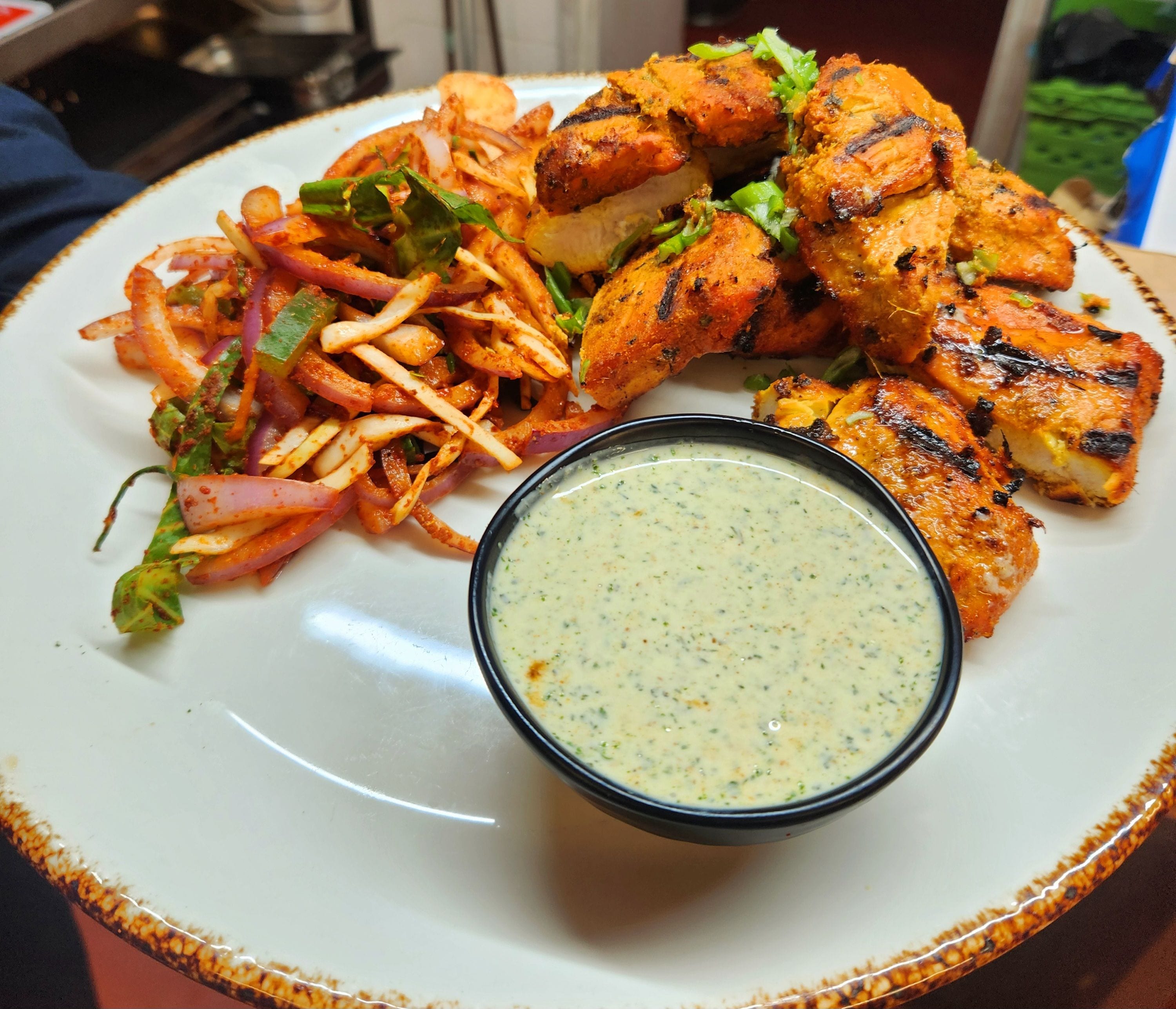 A plate with grilled chicken, a side salad, and a dipping sauce.