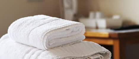 A stack of white towels on a white surface in a hotel room.