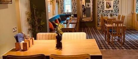 A dining area with a wooden table and chairs, a sofa, and a patterned wall.