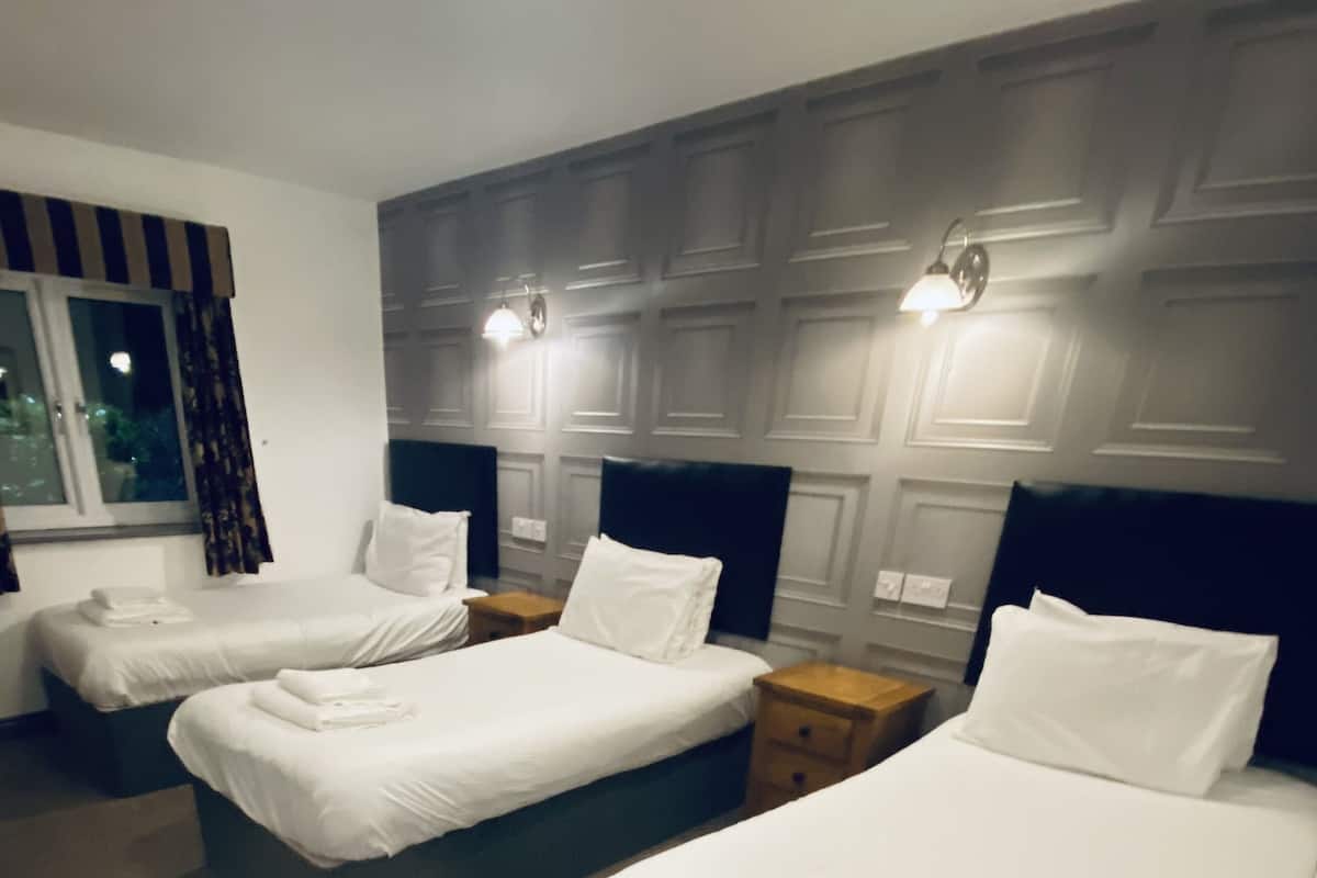 A hotel room with three neatly made beds, each with white linens and pillows, and a window with curtains.