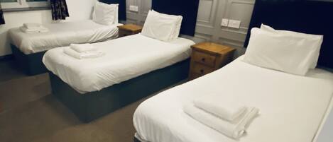 Habitación de hotel con tres camas ordenadas, cada una con ropa blanca y almohadas, y una ventana con cortinas.