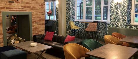 Un espace salon accueillant avec une cheminée en briques, un canapé en cuir et divers types de sièges, notamment des fauteuils et des tables.