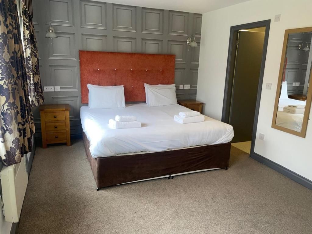 A hotel room with a large bed, a wooden nightstand, a mirror, and a door.