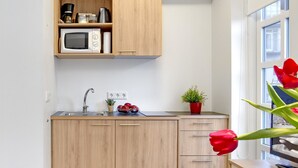 A compact kitchen with wooden cabinets, a microwave, a sink, and a window with a view. - Alfred's Studios (Reykjavik)
