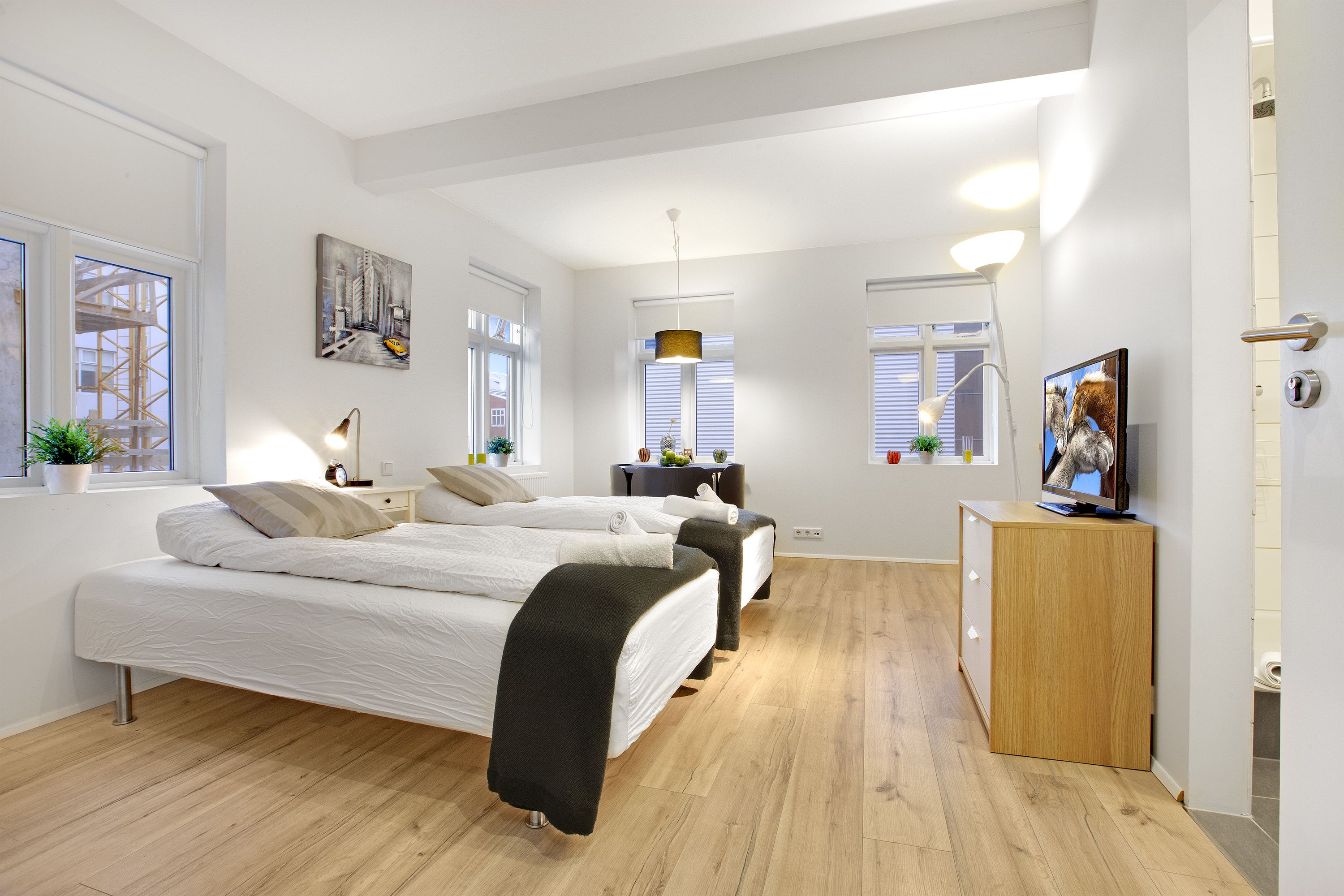 A modern bedroom with two beds, a desk, and a TV.
