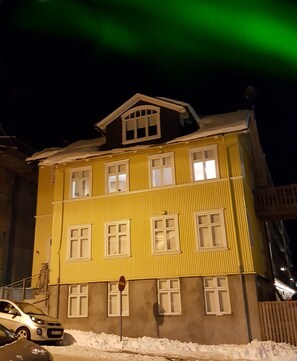 Un edificio amarillo de varios pisos con ventanas de marco blanco y un balcón visible.