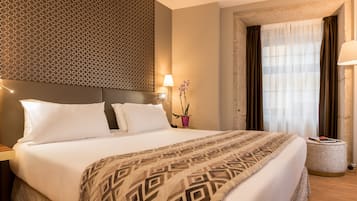 A neatly made bed with a patterned bedspread, a headboard with a geometric design, a bedside lamp, and a window with curtains.