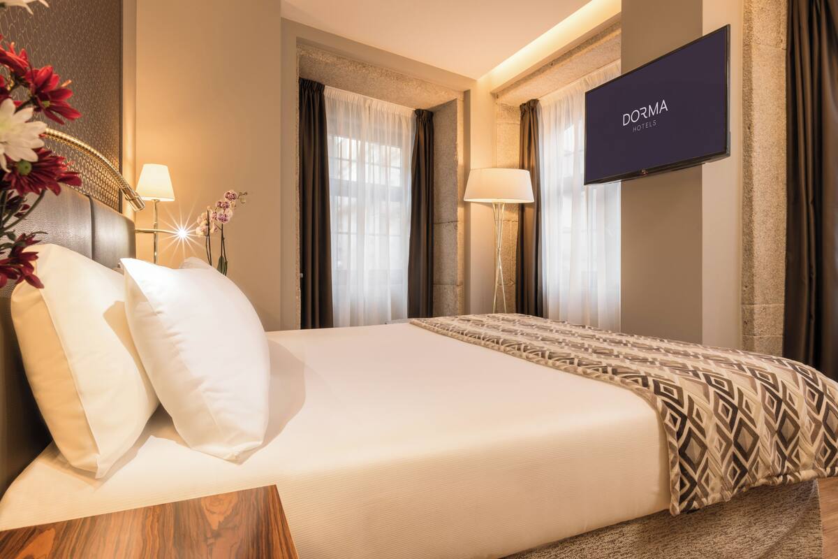 Une chambre d’hôtel avec un lit, deux lampes de chevet, une télévision et un arrangement floral.