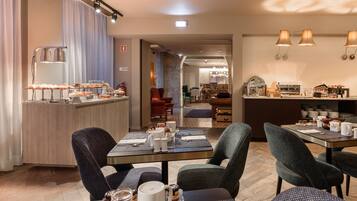 A hotel dining area with tables set for breakfast, a bar with snacks, and a view into the kitchen.