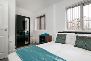 A hotel room with a bed, a wardrobe, a window with blinds, and a view of a building outside.