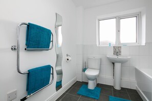 A modern bathroom with a white toilet, a sink, and a bathtub. There are two blue towels hanging on a metal towel rack.
