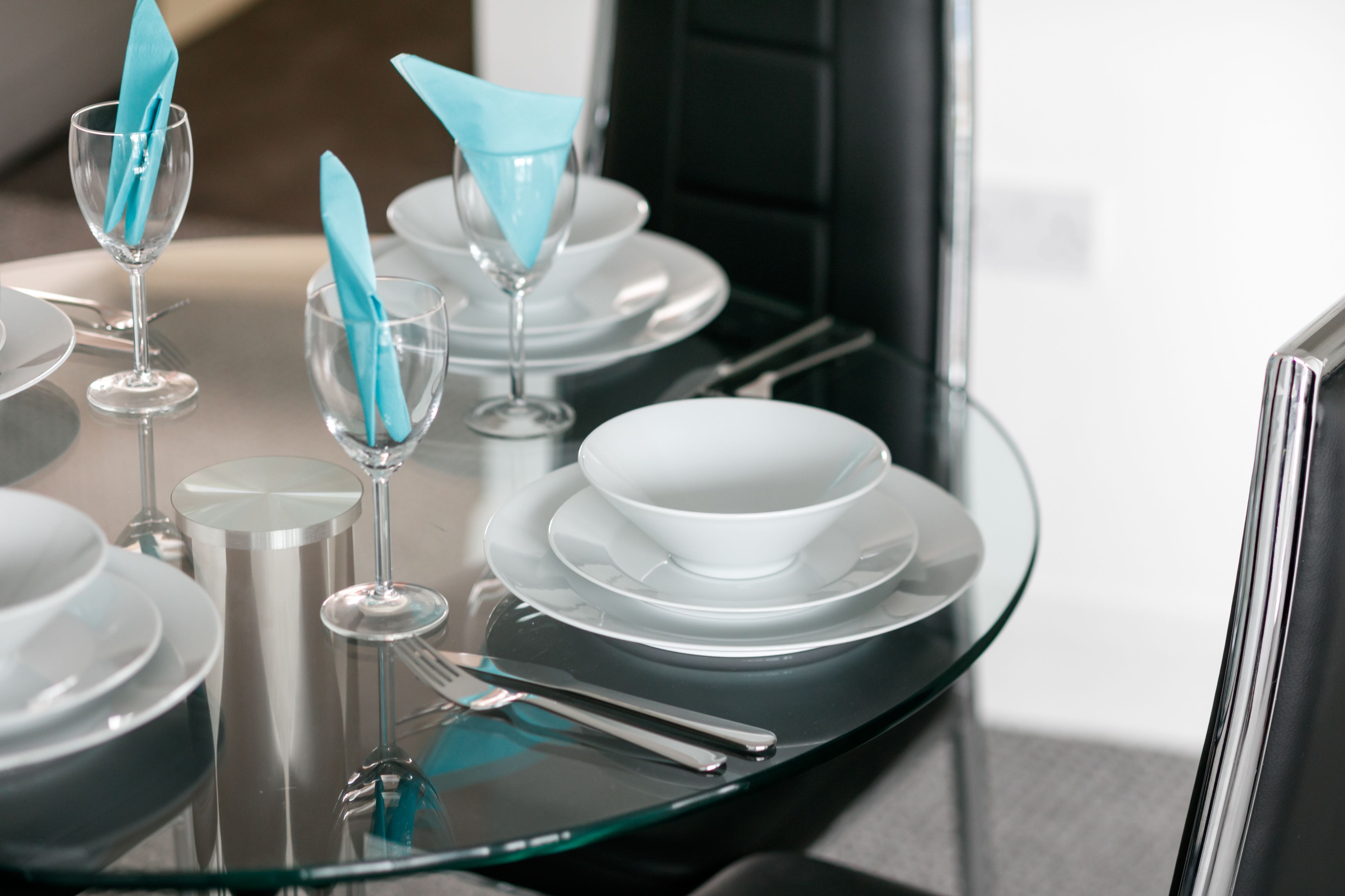 A modern dining table with clear glassware, white plates, and silverware.
