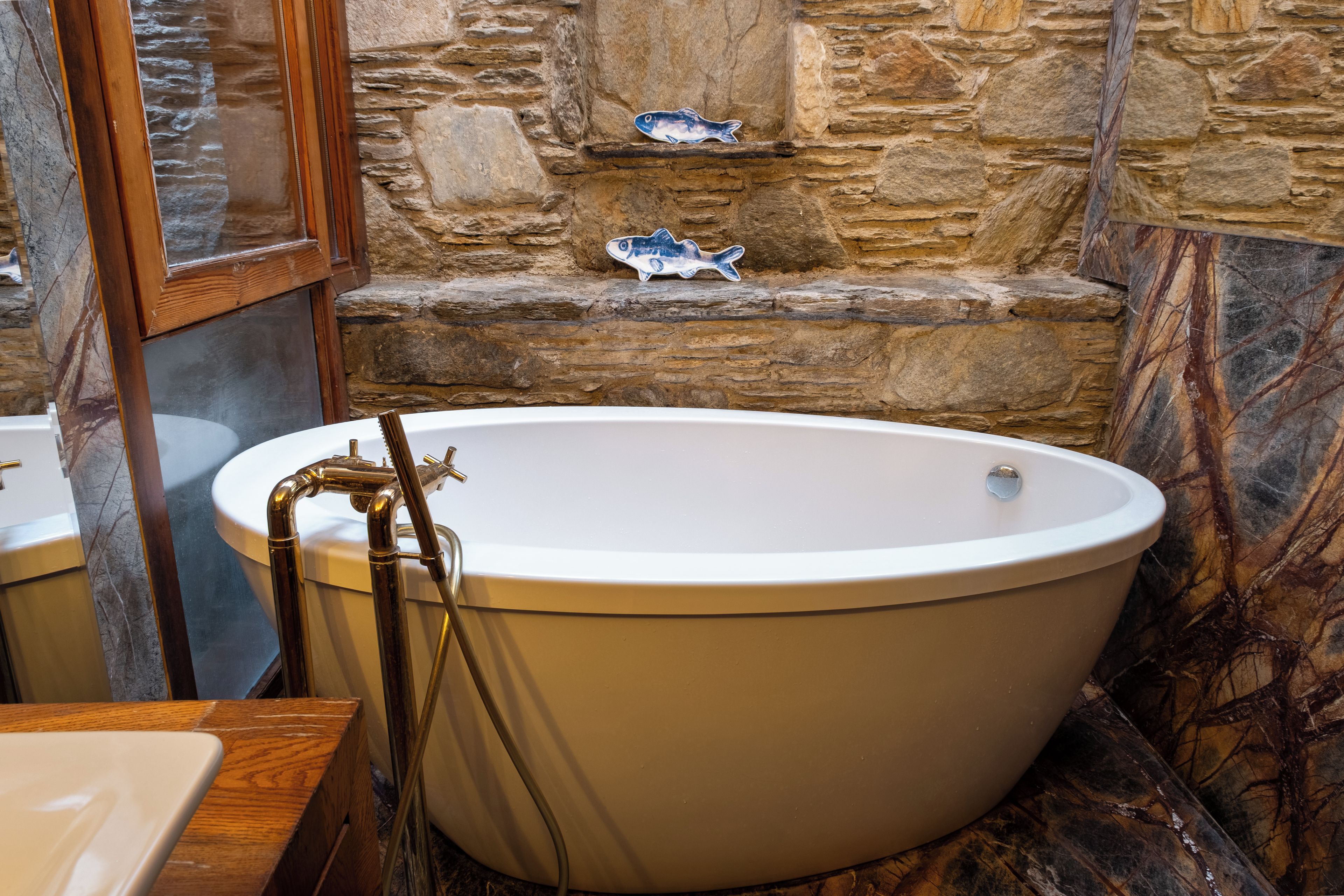 A bathtub in a bathroom with stone walls and a wooden window frame.