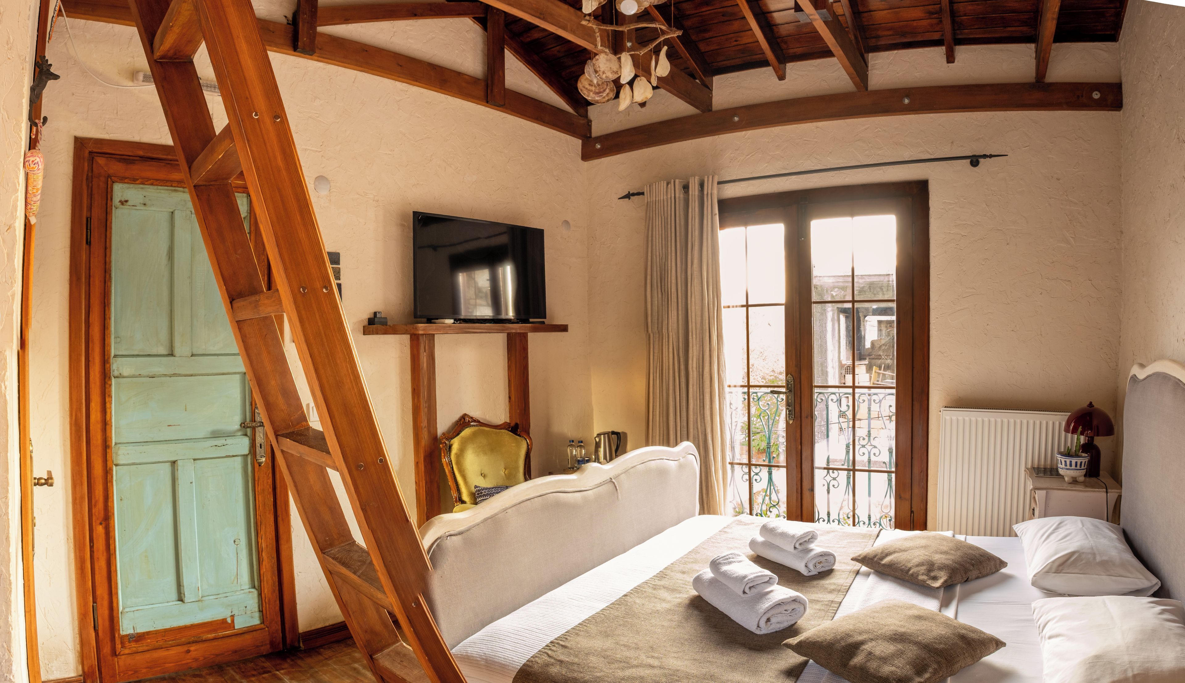 Une chambre avec une échelle en bois, un lit avec des serviettes, une télévision et une fenêtre avec des rideaux.
